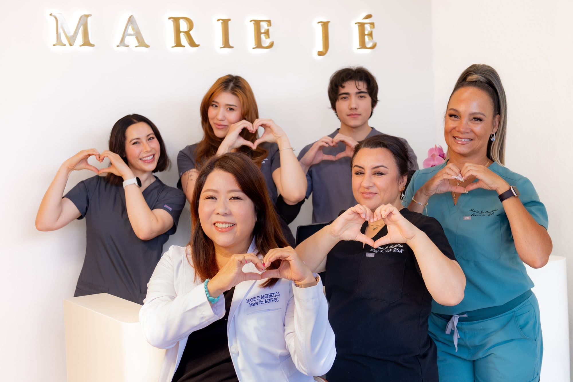 The Marie Jé Aesthetics team making hand hearts under the studio sign
